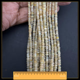May include: A collection of small, pale opal beads in shades of yellow, cream, and white. The beads have a slight shimmer. The strands are approximately 40.6 cm long, as indicated by the ruler at the bottom of the image.