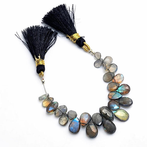 Labradorite faceted pear gemstone bead strand with silk tassels, dark grey with spectacular blue-green flash color, arranged on white background, jewelry making supply bead strand