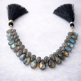 Labradorite faceted pear gemstone bead strand with silk tassels, dark grey with spectacular blue-green flash color, arranged on white background, jewelry making supply bead strand
