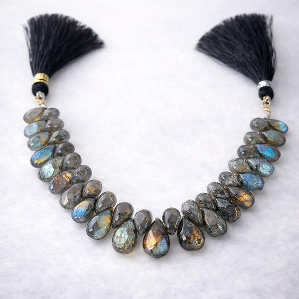 Labradorite faceted pear gemstone bead strand with silk tassels, dark grey with spectacular blue-green flash color, arranged on white background, jewelry making supply bead strand