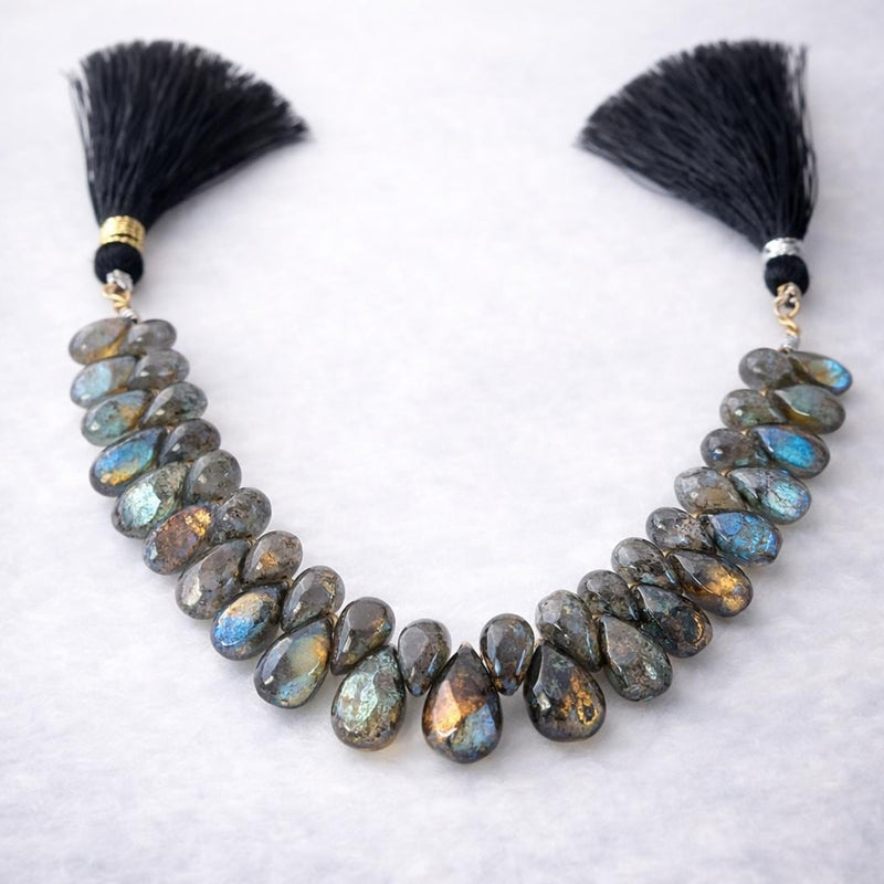 Labradorite faceted pear gemstone bead strand with silk tassels, dark grey with spectacular blue-green flash color, arranged on white background, jewelry making supply bead strand