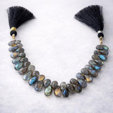 Labradorite faceted teardrop gemstone bead strand with silk tassels, dark grey with spectacular blue-green flash color, arranged on white background, jewelry making supply bead strand